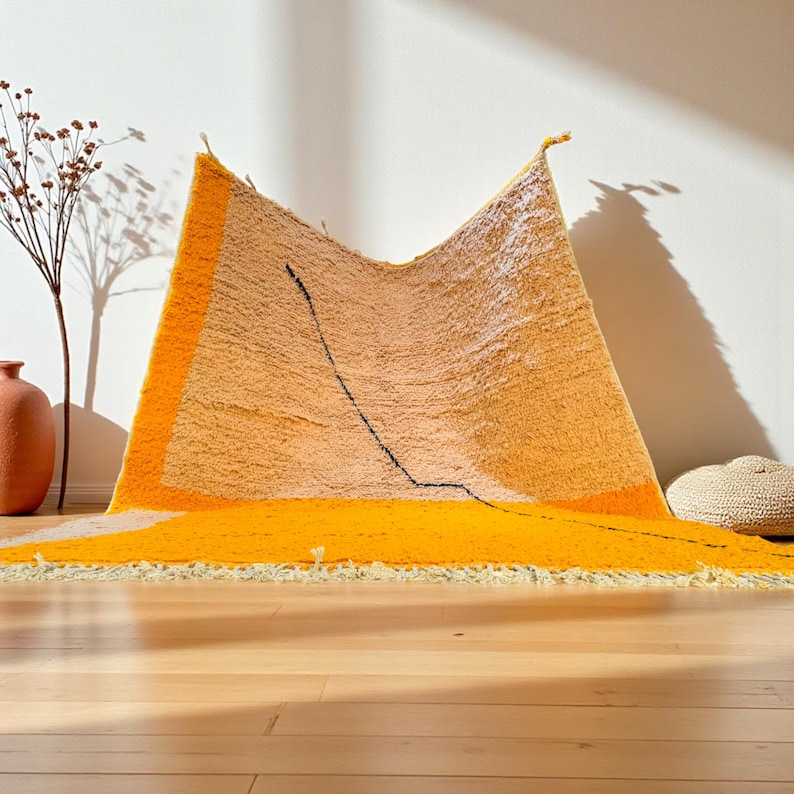 Handmade Moroccan rug in vibrant orange and soft beige with a bold abstract line design. Crafted by Berber artisans using pure wool, this rug combines traditional weaving with a modern artistic touch. Its warm, energetic tones make it a standout for living rooms, creative interiors, or bohemian spaces. Durable, eco-friendly, and soft underfoot, this orange and beige Berber wool carpet adds Moroccan charm and contemporary elegance to any home decor.