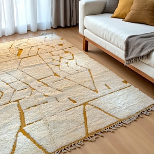 Handmade Moroccan rug in a soft ivory base with striking mustard yellow (Thai Curry) abstract lines. Woven by Berber artisans in pure wool, this rug blends tradition and modern style. Its geometric tribal pattern and warm tones make it perfect for living rooms, bedrooms, or creative interiors. Durable, eco-friendly, and soft underfoot, this ivory and mustard Berber carpet adds Moroccan charm and luxury to boho, modern, or eclectic home decor.
