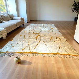 Handmade Moroccan rug in a soft ivory base with striking mustard yellow (Thai Curry) abstract lines. Woven by Berber artisans in pure wool, this rug blends tradition and modern style. Its geometric tribal pattern and warm tones make it perfect for living rooms, bedrooms, or creative interiors. Durable, eco-friendly, and soft underfoot, this ivory and mustard Berber carpet adds Moroccan charm and luxury to boho, modern, or eclectic home decor.