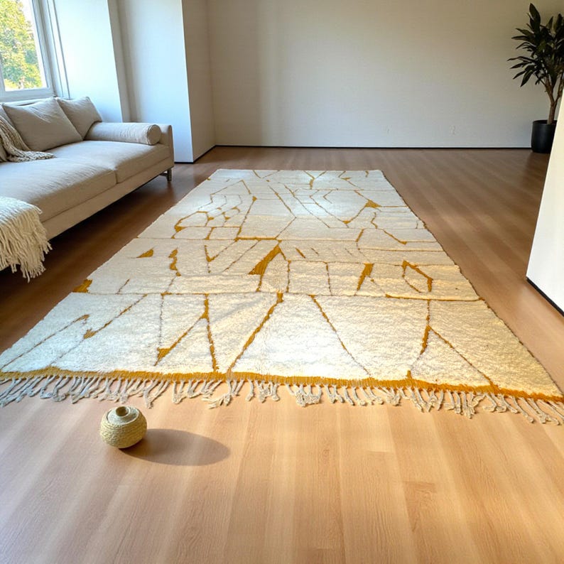 Handmade Moroccan rug in a soft ivory base with striking mustard yellow (Thai Curry) abstract lines. Woven by Berber artisans in pure wool, this rug blends tradition and modern style. Its geometric tribal pattern and warm tones make it perfect for living rooms, bedrooms, or creative interiors. Durable, eco-friendly, and soft underfoot, this ivory and mustard Berber carpet adds Moroccan charm and luxury to boho, modern, or eclectic home decor.