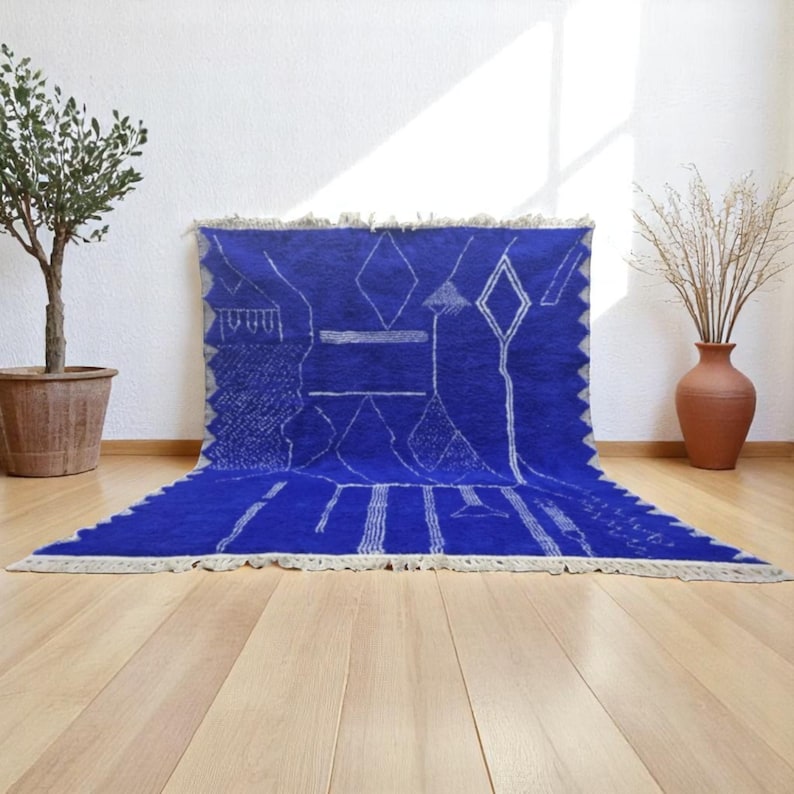 Striking handmade Moroccan rug in bold cobalt blue with white tribal Amazigh symbols. Crafted from natural wool, this unique Berber rug features traditional abstract lines and diamond motifs, perfect for adding a splash of color and culture to modern interiors. Ideal for boho, eclectic, or contemporary homes looking for a statement piece. Soft texture and timeless authenticity.