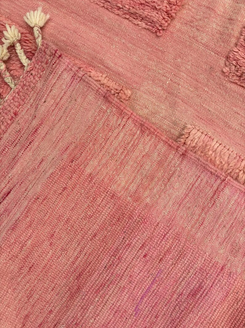 Handwoven Moroccan wool area rug in soft solid pink with a plush, high-pile texture and natural cream wool fringes. Made by Amazigh artisans in the Atlas Mountains, this minimalist Beni Ourain-style rug brings warmth, softness, and authentic Moroccan craftsmanship to modern boho or minimalist interiors.
