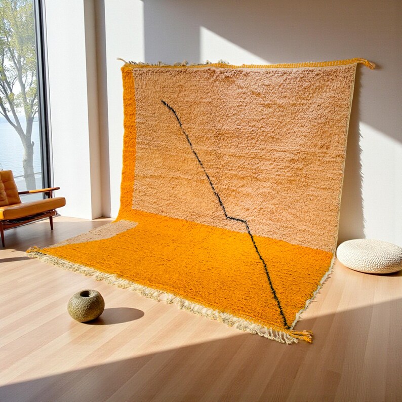 Handmade Moroccan rug in vibrant orange and soft beige with a bold abstract line design. Crafted by Berber artisans using pure wool, this rug combines traditional weaving with a modern artistic touch. Its warm, energetic tones make it a standout for living rooms, creative interiors, or bohemian spaces. Durable, eco-friendly, and soft underfoot, this orange and beige Berber wool carpet adds Moroccan charm and contemporary elegance to any home decor.