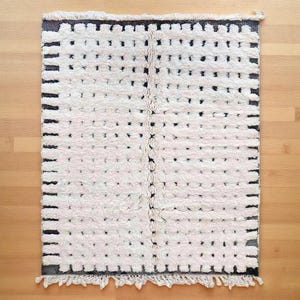 Handmade Moroccan wool rug featuring a warm ivory background with gray borders, short linear accents, and small irregular dotted motifs arranged across the surface. Individually hand-knotted by skilled Amazigh artisans in the Atlas Mountains using 100% natural sheep wool, its thick plush high pile adds softness, warmth, and authentic handcrafted texture. Finished with natural ivory fringes, this refined rug organic modern, Japandi, minimalist, Scandinavian, contemporary, and neutral interiors.