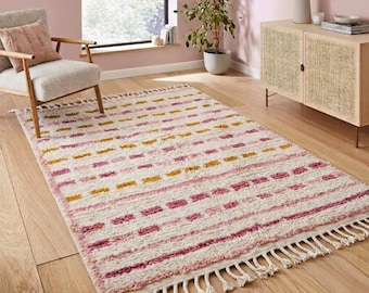 Può includere: Un tappeto rettangolare con base color crema e file orizzontali di motivi tratteggiati nelle tonalità del rosa, magenta e giallo senape. Il tappeto presenta un pelo strutturato ed è rifinito con lunghe frange color crema su entrambe le estremità.