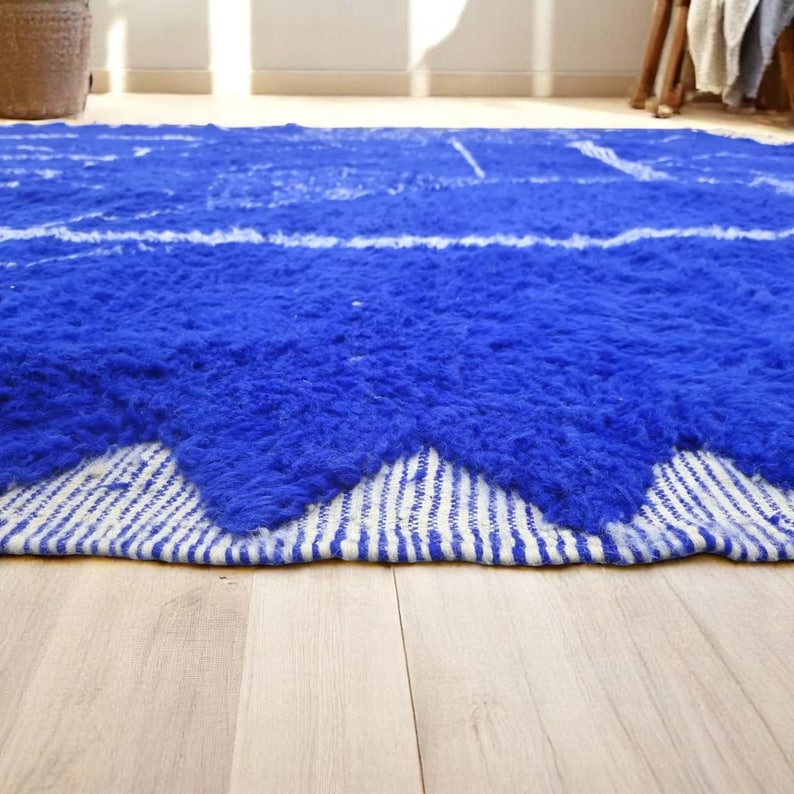 Striking handmade Moroccan rug in bold cobalt blue with white tribal Amazigh symbols. Crafted from natural wool, this unique Berber rug features traditional abstract lines and diamond motifs, perfect for adding a splash of color and culture to modern interiors. Ideal for boho, eclectic, or contemporary homes looking for a statement piece. Soft texture and timeless authenticity.