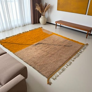 Handmade Moroccan rug in vibrant orange and soft beige with a bold abstract line design. Crafted by Berber artisans using pure wool, this rug combines traditional weaving with a modern artistic touch. Its warm, energetic tones make it a standout for living rooms, creative interiors, or bohemian spaces. Durable, eco-friendly, and soft underfoot, this orange and beige Berber wool carpet adds Moroccan charm and contemporary elegance to any home decor.