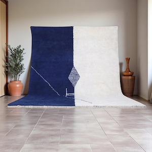 Handmade Moroccan wool rug in navy blue and ivory with a bold split design and fine geometric detailing. Handwoven by Berber artisans in Morocco using 100% natural wool, this rug is soft, eco-friendly, and durable. The modern minimalist design brings elegance and contrast to living rooms, bedrooms, or offices. Its clean color palette pairs effortlessly with neutral or bold interiors, making it a versatile statement piece. Finished with hand-knotted fringes for authenticity.