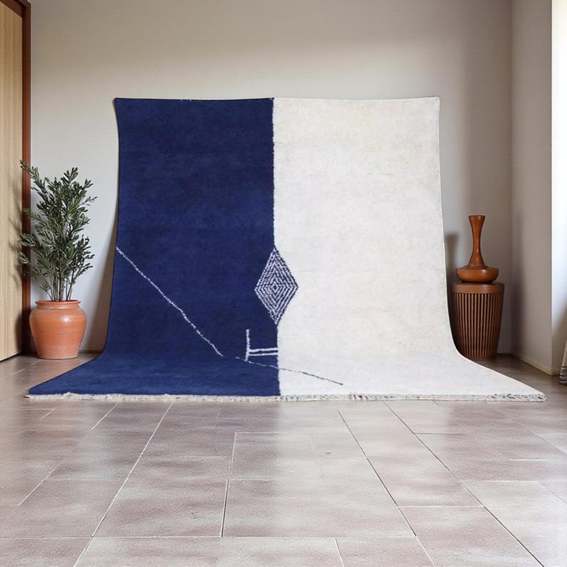 Handmade Moroccan wool rug in navy blue and ivory with a bold split design and fine geometric detailing. Handwoven by Berber artisans in Morocco using 100% natural wool, this rug is soft, eco-friendly, and durable. The modern minimalist design brings elegance and contrast to living rooms, bedrooms, or offices. Its clean color palette pairs effortlessly with neutral or bold interiors, making it a versatile statement piece. Finished with hand-knotted fringes for authenticity.