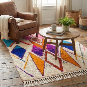 Authentic handmade Moroccan Boujaad rug featuring bold geometric diamond patterns in vibrant multicolor — electric blue, fuchsia pink, orange, yellow and purple on ivory wool background. Hand-knotted by Berber artisans in Morocco using natural wool. Perfect boho statement rug for living room, bedroom or dining room. One-of-a-kind colorful area rug with traditional fringe.
