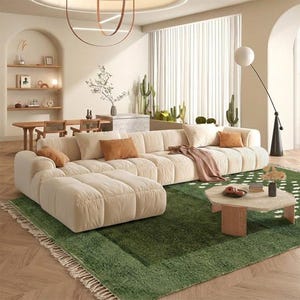A plush handwoven Moroccan Berber rug in a rich moss green. The thick wool carpet features a solid dark green band near the top and a lighter mossy green base beautifully adorned with small, cream-colored geometric diamond motifs at the bottom. It is draped elegantly against a white painted brick wall next to a gold accent table with trailing ivy, perfectly capturing a warm, earthy, and organic modern interior design aesthetic.
