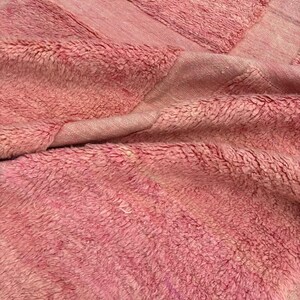 Handwoven Moroccan wool area rug in soft solid pink with a plush, high-pile texture and natural cream wool fringes. Made by Amazigh artisans in the Atlas Mountains, this minimalist Beni Ourain-style rug brings warmth, softness, and authentic Moroccan craftsmanship to modern boho or minimalist interiors.