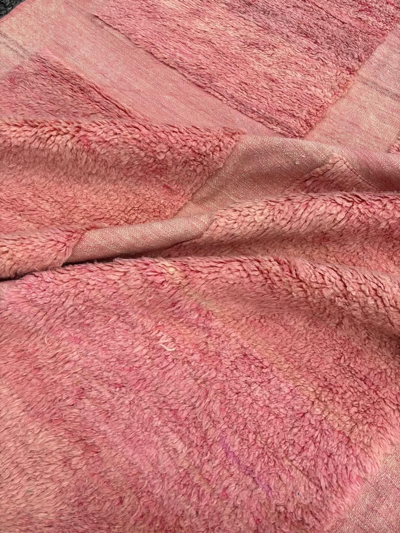 Handwoven Moroccan wool area rug in soft solid pink with a plush, high-pile texture and natural cream wool fringes. Made by Amazigh artisans in the Atlas Mountains, this minimalist Beni Ourain-style rug brings warmth, softness, and authentic Moroccan craftsmanship to modern boho or minimalist interiors.