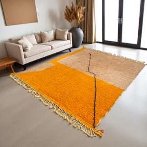 Handmade Moroccan rug in vibrant orange and soft beige with a bold abstract line design. Crafted by Berber artisans using pure wool, this rug combines traditional weaving with a modern artistic touch. Its warm, energetic tones make it a standout for living rooms, creative interiors, or bohemian spaces. Durable, eco-friendly, and soft underfoot, this orange and beige Berber wool carpet adds Moroccan charm and contemporary elegance to any home decor.
