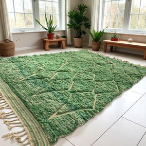 Green Moroccan wool rug with cream diamond lattice pattern, handmade in Beni Ourain style. Styled in a bright modern boho room with plants, rattan furniture, and natural light. The rug has a plush texture, tribal design, and fringe details, making it perfect for earthy, creative, or minimalist interiors. Crafted by Berber artisans, it's soft, thick, and ethically made using traditional weaving techniques.