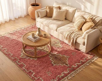 Può includere: Un tappeto rettangolare con una base rosa intenso e un motivo centrale a rombi in tonalità marrone e crema tenue. Il tappeto presenta una consistenza a pelo lungo e spesso, ed è rifinito con lunghe frange annodate sui due lati corti.