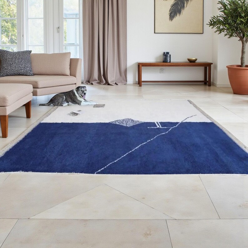 Handmade Moroccan wool rug in navy blue and ivory with a bold split design and fine geometric detailing. Handwoven by Berber artisans in Morocco using 100% natural wool, this rug is soft, eco-friendly, and durable. The modern minimalist design brings elegance and contrast to living rooms, bedrooms, or offices. Its clean color palette pairs effortlessly with neutral or bold interiors, making it a versatile statement piece. Finished with hand-knotted fringes for authenticity.