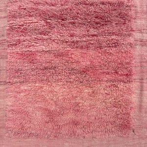 Handwoven Moroccan wool area rug in soft solid pink with a plush, high-pile texture and natural cream wool fringes. Made by Amazigh artisans in the Atlas Mountains, this minimalist Beni Ourain-style rug brings warmth, softness, and authentic Moroccan craftsmanship to modern boho or minimalist interiors.