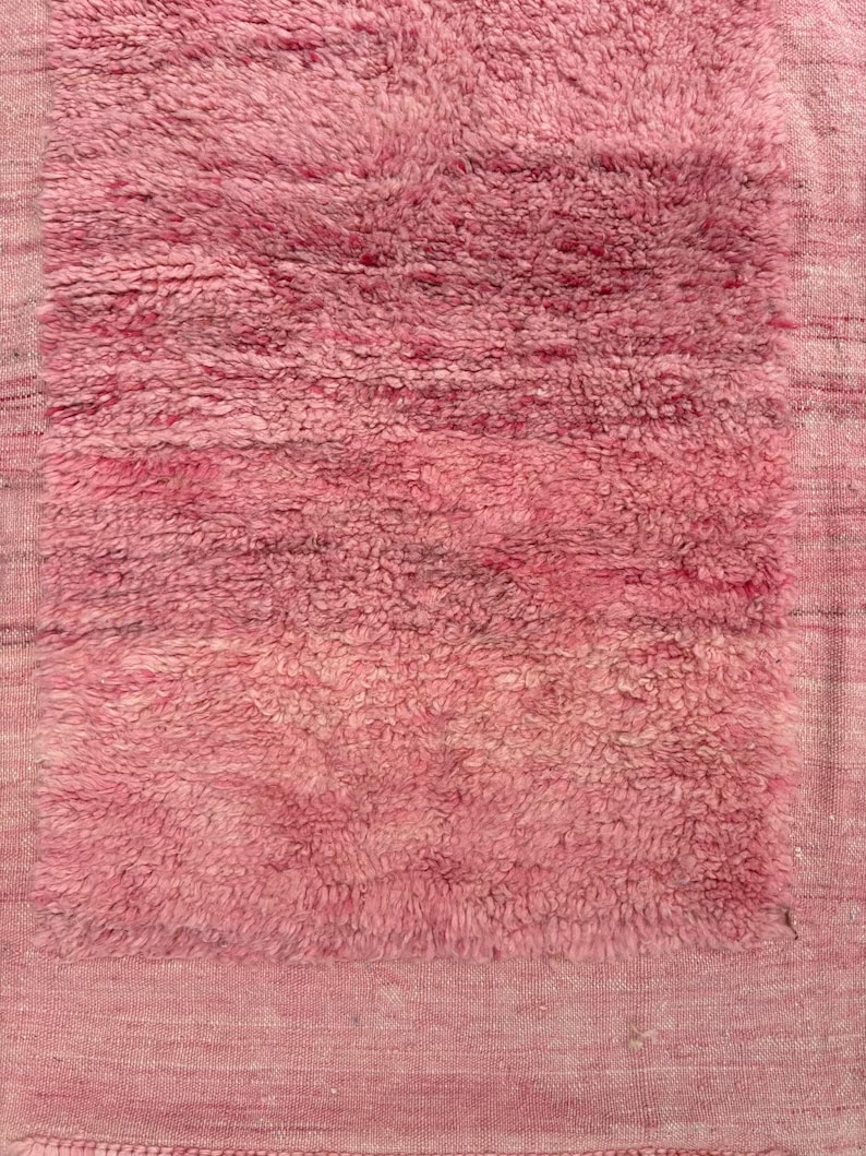 Handwoven Moroccan wool area rug in soft solid pink with a plush, high-pile texture and natural cream wool fringes. Made by Amazigh artisans in the Atlas Mountains, this minimalist Beni Ourain-style rug brings warmth, softness, and authentic Moroccan craftsmanship to modern boho or minimalist interiors.