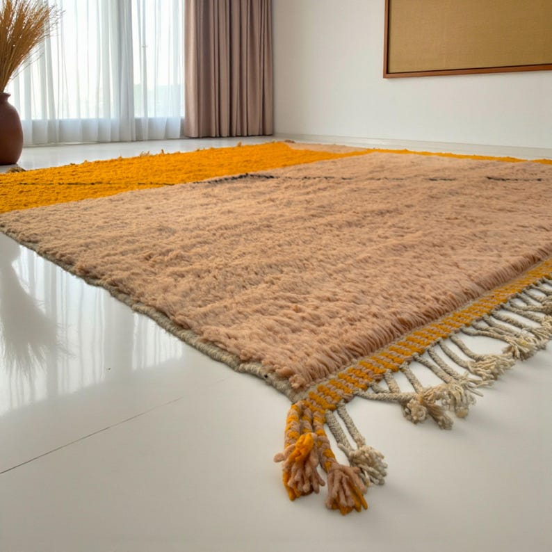 Handmade Moroccan rug in vibrant orange and soft beige with a bold abstract line design. Crafted by Berber artisans using pure wool, this rug combines traditional weaving with a modern artistic touch. Its warm, energetic tones make it a standout for living rooms, creative interiors, or bohemian spaces. Durable, eco-friendly, and soft underfoot, this orange and beige Berber wool carpet adds Moroccan charm and contemporary elegance to any home decor.