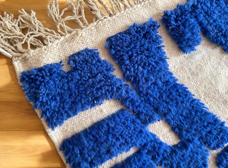 A vintage Moroccan wool rug with a bold blue abstract design handwoven on a neutral beige background, featuring plush texture and traditional fringed edges Vintage Rug, Moroccan Rug Wool Rug Abstract Rug Handwoven Rug Blue Rug Bold Design Modern Rug