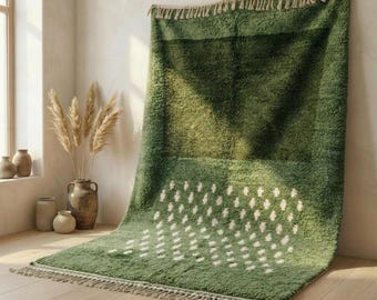 May include: A green rug with a textured surface and a geometric pattern of white diamond shapes. The rug has a fringe along the bottom edge and is leaning against a wall. The rug is made of a soft, plush material.