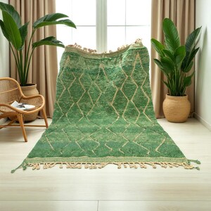 Green Moroccan wool rug with cream diamond lattice pattern, handmade in Beni Ourain style. Styled in a bright modern boho room with plants, rattan furniture, and natural light. The rug has a plush texture, tribal design, and fringe details, making it perfect for earthy, creative, or minimalist interiors. Crafted by Berber artisans, it's soft, thick, and ethically made using traditional weaving techniques.