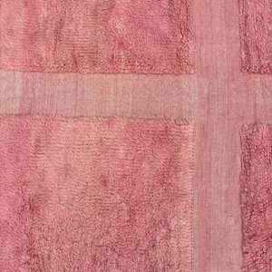 Handwoven Moroccan wool area rug in soft solid pink with a plush, high-pile texture and natural cream wool fringes. Made by Amazigh artisans in the Atlas Mountains, this minimalist Beni Ourain-style rug brings warmth, softness, and authentic Moroccan craftsmanship to modern boho or minimalist interiors.