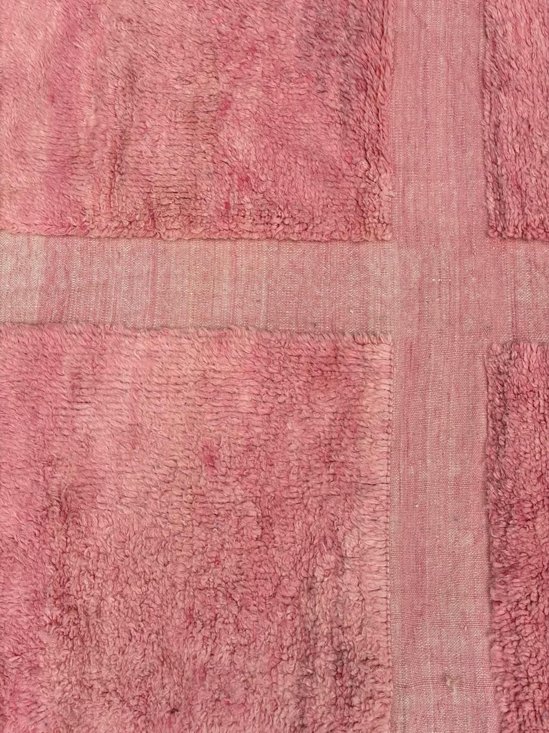 Handwoven Moroccan wool area rug in soft solid pink with a plush, high-pile texture and natural cream wool fringes. Made by Amazigh artisans in the Atlas Mountains, this minimalist Beni Ourain-style rug brings warmth, softness, and authentic Moroccan craftsmanship to modern boho or minimalist interiors.