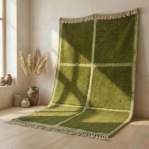 May include: A green rectangular rug with a grid pattern and fringe trim. The rug is made of a soft, textured material and is displayed on a wooden floor. The rug is approximately 152 cm wide and 203 cm long.