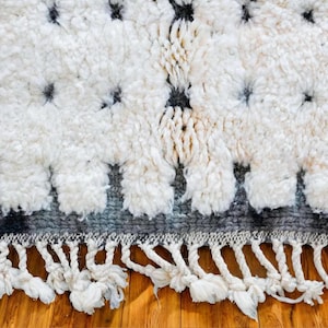 Handmade Moroccan rug in black and white with a dotted Berber pattern and bold black stripe edges. Crafted from natural wool by artisans in the Atlas Mountains, this rug combines authenticity and modern design. Perfect for boho chic, Scandinavian, and minimalist interiors, it brings warmth, texture, and elegance to living rooms, bedrooms, and creative spaces. A luxury Moroccan wool carpet that blends artisanal tradition with contemporary home decor style.