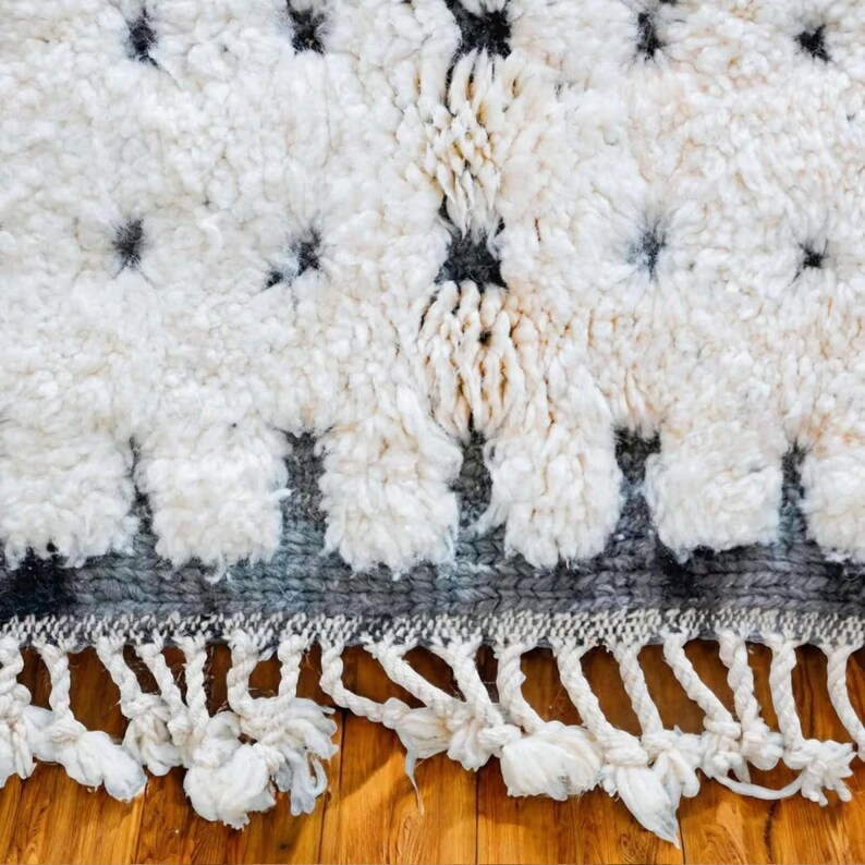Handmade Moroccan rug in black and white with a dotted Berber pattern and bold black stripe edges. Crafted from natural wool by artisans in the Atlas Mountains, this rug combines authenticity and modern design. Perfect for boho chic, Scandinavian, and minimalist interiors, it brings warmth, texture, and elegance to living rooms, bedrooms, and creative spaces. A luxury Moroccan wool carpet that blends artisanal tradition with contemporary home decor style.