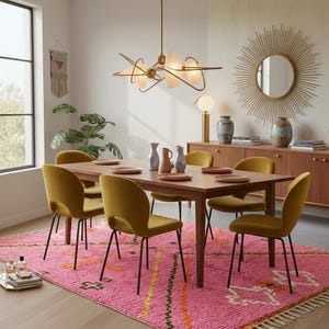 A plush, handwoven Moroccan Boujad rug featuring a vibrant hot pink base adorned with neon orange crosses, white diamonds, and green zigzag geometric patterns. The brightly colored wool carpet is draped elegantly against a white painted brick wall next to a gold accent table with pink pillar candles, perfectly capturing a playful maximalist and dopamine decor aesthetic.