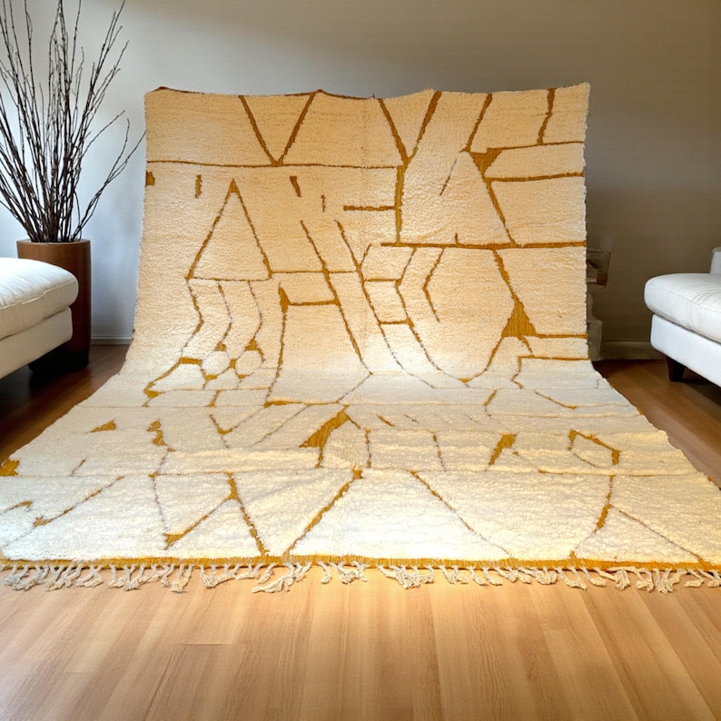 Handmade Moroccan rug in a soft ivory base with striking mustard yellow (Thai Curry) abstract lines. Woven by Berber artisans in pure wool, this rug blends tradition and modern style. Its geometric tribal pattern and warm tones make it perfect for living rooms, bedrooms, or creative interiors. Durable, eco-friendly, and soft underfoot, this ivory and mustard Berber carpet adds Moroccan charm and luxury to boho, modern, or eclectic home decor.
