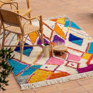 Authentic handmade Moroccan Boujaad rug featuring bold geometric diamond patterns in vibrant multicolor — electric blue, fuchsia pink, orange, yellow and purple on ivory wool background. Hand-knotted by Berber artisans in Morocco using natural wool. Perfect boho statement rug for living room, bedroom or dining room. One-of-a-kind colorful area rug with traditional fringe.
