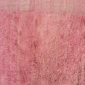 Handwoven Moroccan wool area rug in soft solid pink with a plush, high-pile texture and natural cream wool fringes. Made by Amazigh artisans in the Atlas Mountains, this minimalist Beni Ourain-style rug brings warmth, softness, and authentic Moroccan craftsmanship to modern boho or minimalist interiors.