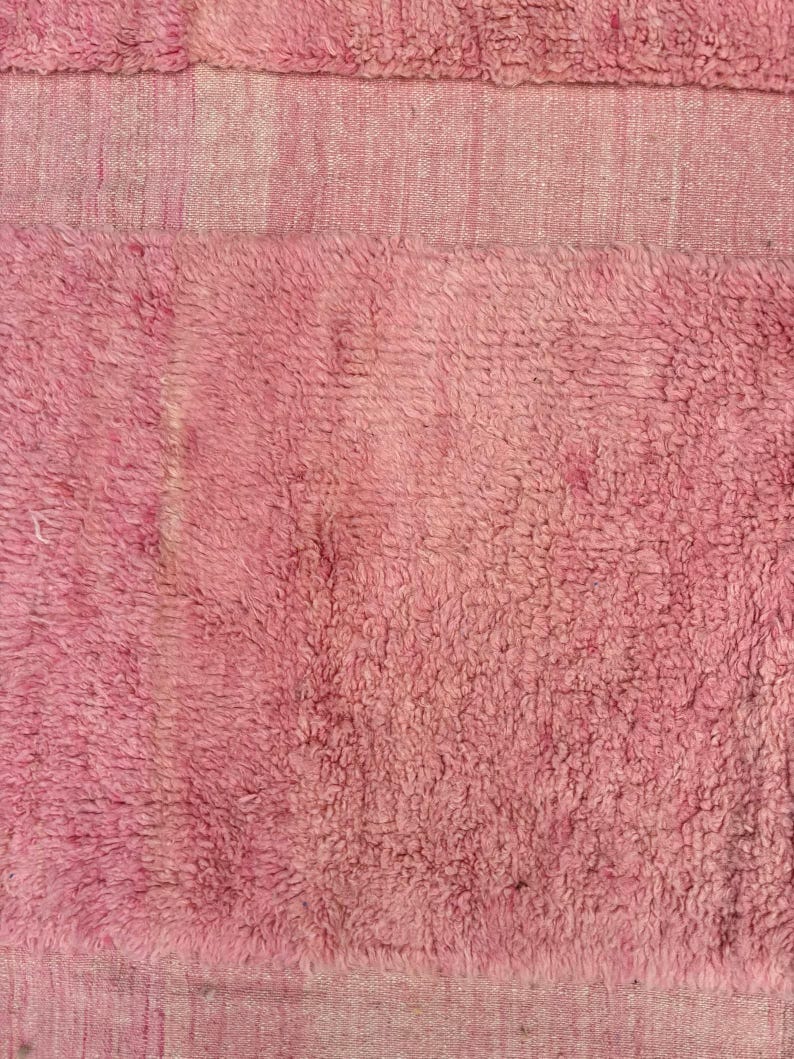 Handwoven Moroccan wool area rug in soft solid pink with a plush, high-pile texture and natural cream wool fringes. Made by Amazigh artisans in the Atlas Mountains, this minimalist Beni Ourain-style rug brings warmth, softness, and authentic Moroccan craftsmanship to modern boho or minimalist interiors.