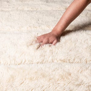 Beautiful handmade Moroccan rug in beige and black, featuring a bold geometric diamond pattern. Crafted from soft wool, it adds warmth and style to living rooms, bedrooms, or boho-chic spaces. Unique fringes enhance its artisan charm and timeless