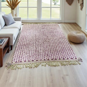 Handwoven Moroccan wool rug in wistful mauve and cream tones. Features a soft geometric pattern with textured pile and hand-knotted fringes. Perfect for living rooms, bedrooms, or boho interiors. Made from 100% natural wool by Berber artisans in Morocco. This handmade rug adds warmth, elegance, and Moroccan authenticity to modern or vintage-style spaces.