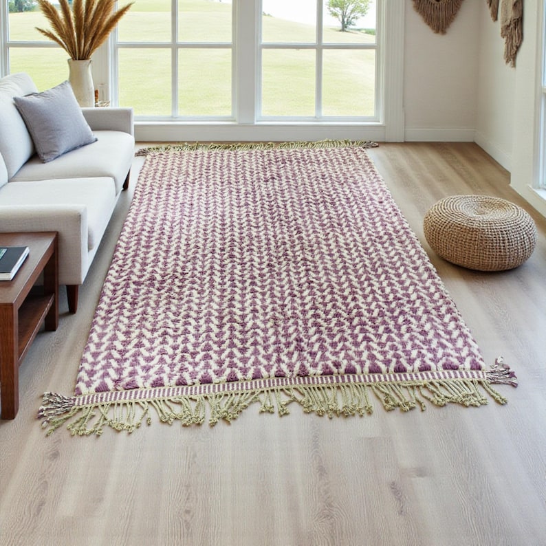 Handwoven Moroccan wool rug in wistful mauve and cream tones. Features a soft geometric pattern with textured pile and hand-knotted fringes. Perfect for living rooms, bedrooms, or boho interiors. Made from 100% natural wool by Berber artisans in Morocco. This handmade rug adds warmth, elegance, and Moroccan authenticity to modern or vintage-style spaces.