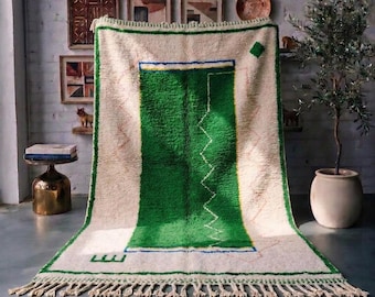 Può includere: Un tappeto rettangolare con sfondo color crema e un grande blocco centrale rettangolare verde smeraldo. Il tappeto presenta un sottile bordo blu, una linea bianca a zigzag e un accento a forma di diamante verde, rifinito con frange color crema.