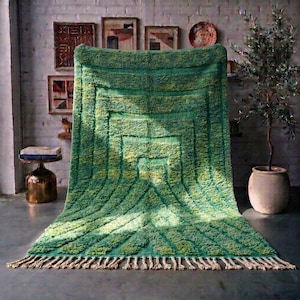 May include: A rectangular area rug featuring a deep green and lime green shag texture with a concentric geometric pattern of raised lines. The rug has a thick pile and is finished with a row of light beige knotted fringe along the bottom edge.