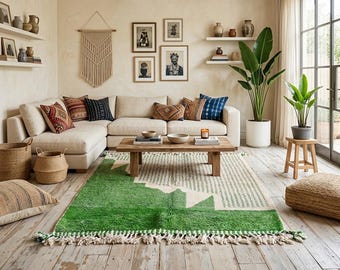 May include: A living room featuring a cream sectional sofa with patterned throw pillows, a wooden coffee table, and a green and cream geometric area rug with fringe. The space includes wall shelves, framed art, a macrame wall hanging, and plants.