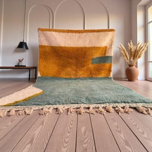 Può includere: Un tappeto geometrico e colorato con un morbido pelo strutturato. Il tappeto presenta un design con sezioni giallo senape, azzurro e crema. Il tappeto ha una frangia sul bordo inferiore.