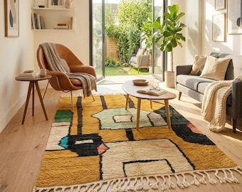 Può includere: Un tappeto rettangolare con base giallo senape e motivi geometrici in nero, crema, verde chiaro e blu. Il tappeto presenta una consistenza spessa e folta, rifinita con lunghe frange annodate color crema su entrambi i lati corti.