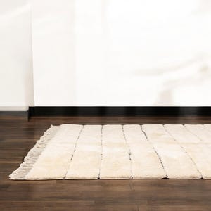 Handmade Moroccan rug with minimalist horizontal striped design, crafted from plush wool in a warm beige tone. Soft and cozy, this rug is ideal for living rooms, bedrooms, or modern spaces. Subtle fringes add a touch of traditional elegance.