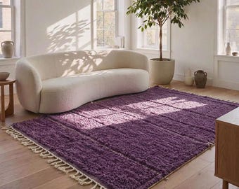 Può includere: Un tappeto rettangolare di una tonalità viola intenso caratterizzato da una consistenza spessa e pelosa, con frange annodate color crema lungo i bordi più corti. Il tappeto è posizionato su un pavimento in legno chiaro e ha un pelo uniforme.