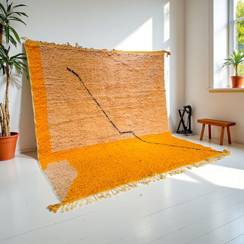Handmade Moroccan rug in vibrant orange and soft beige with a bold abstract line design. Crafted by Berber artisans using pure wool, this rug combines traditional weaving with a modern artistic touch. Its warm, energetic tones make it a standout for living rooms, creative interiors, or bohemian spaces. Durable, eco-friendly, and soft underfoot, this orange and beige Berber wool carpet adds Moroccan charm and contemporary elegance to any home decor.