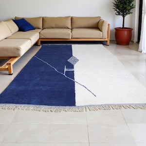 Handmade Moroccan wool rug in navy blue and ivory with a bold split design and fine geometric detailing. Handwoven by Berber artisans in Morocco using 100% natural wool, this rug is soft, eco-friendly, and durable. The modern minimalist design brings elegance and contrast to living rooms, bedrooms, or offices. Its clean color palette pairs effortlessly with neutral or bold interiors, making it a versatile statement piece. Finished with hand-knotted fringes for authenticity.
