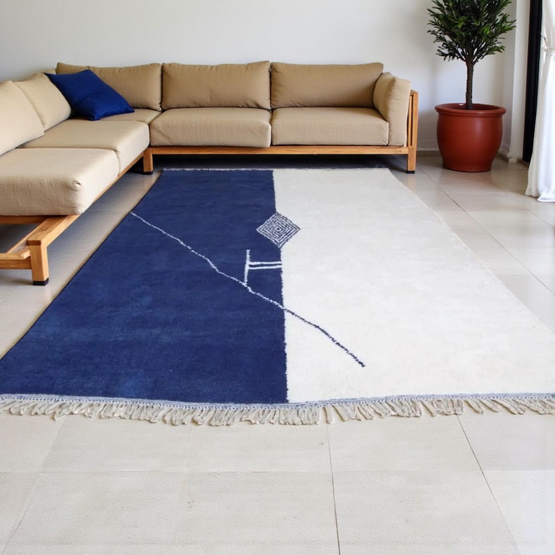 Handmade Moroccan wool rug in navy blue and ivory with a bold split design and fine geometric detailing. Handwoven by Berber artisans in Morocco using 100% natural wool, this rug is soft, eco-friendly, and durable. The modern minimalist design brings elegance and contrast to living rooms, bedrooms, or offices. Its clean color palette pairs effortlessly with neutral or bold interiors, making it a versatile statement piece. Finished with hand-knotted fringes for authenticity.